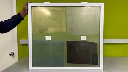 samples of BDF, G Greenfilm, Gila, and Coavas Temperature Control Window Films on window sitting on table, hand holding window upright